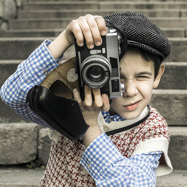 boy using an old vintage camera outside a building